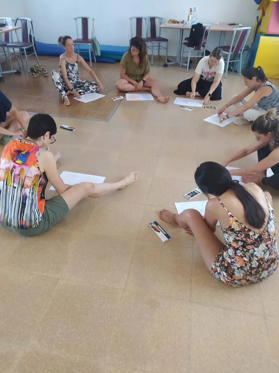 Mestres assegudes a terra, en cercle, compartint els seus dibuixos.