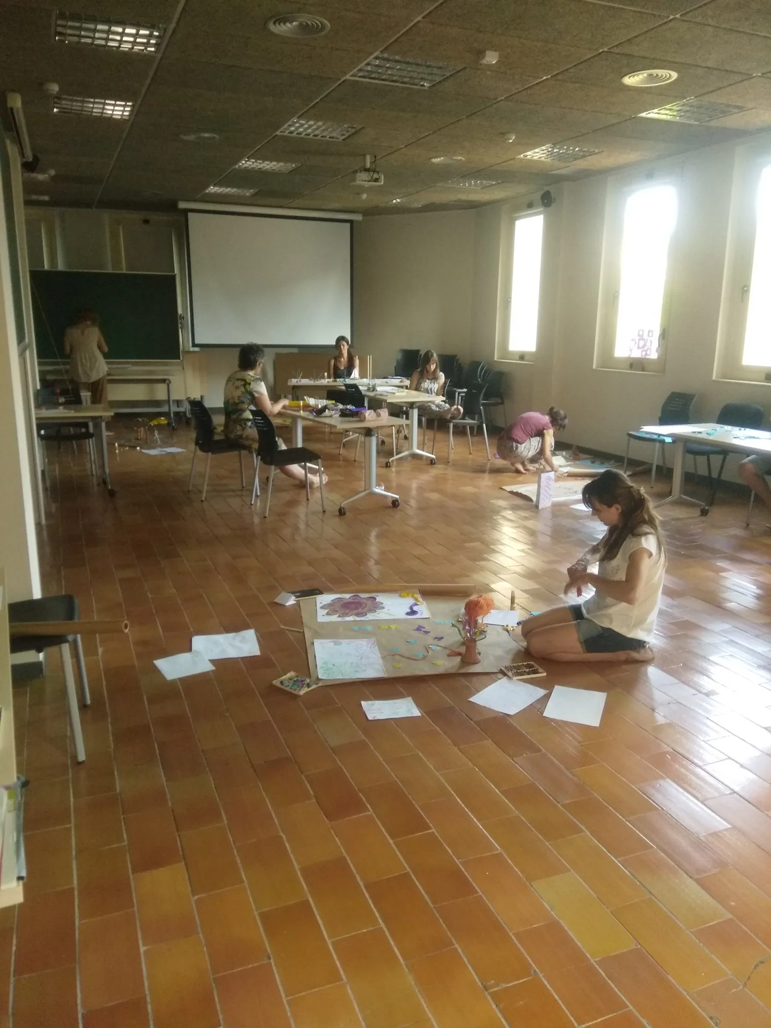 Participants creant a terra sobre grans papers en una sala lluminosa.