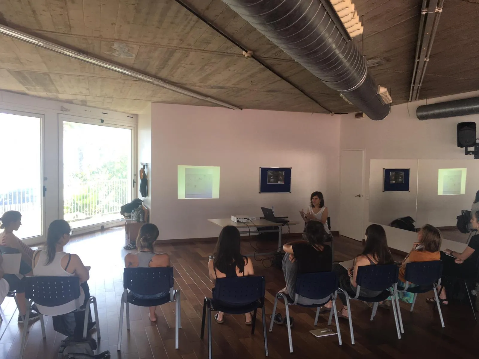 Grup assegut en rotllana en una sala àmplia amb finestrals durant el curs d'introducció a l'artteràpia.