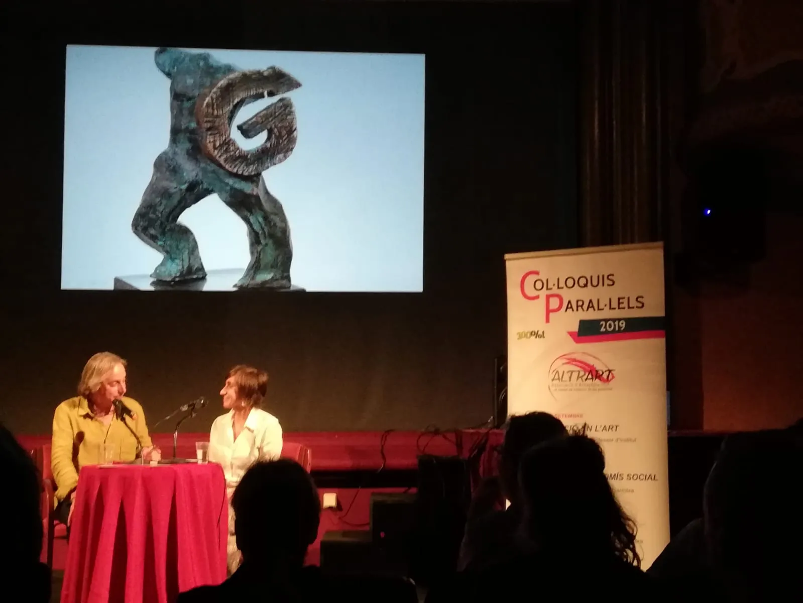 Entrevista a Narcís Coderch a l'escenari amb la projecció d'una escultura.