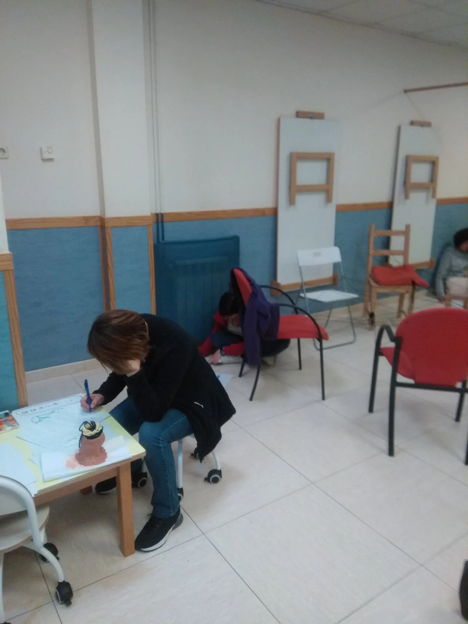 Una educadora dibuixant asseguda en una cadira baixa.