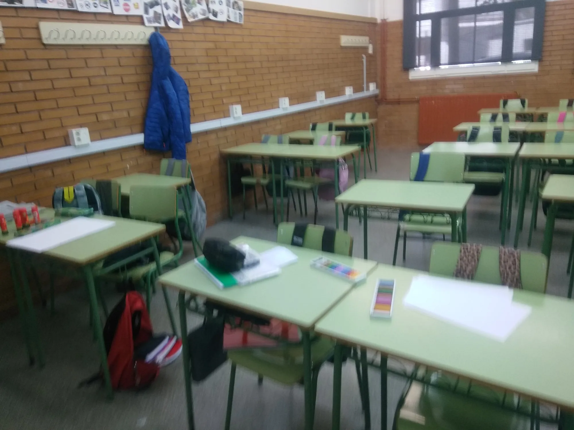 Aula d'institut amb pupitres preparats amb fulls i materials per a la sessió d'artteràpia.