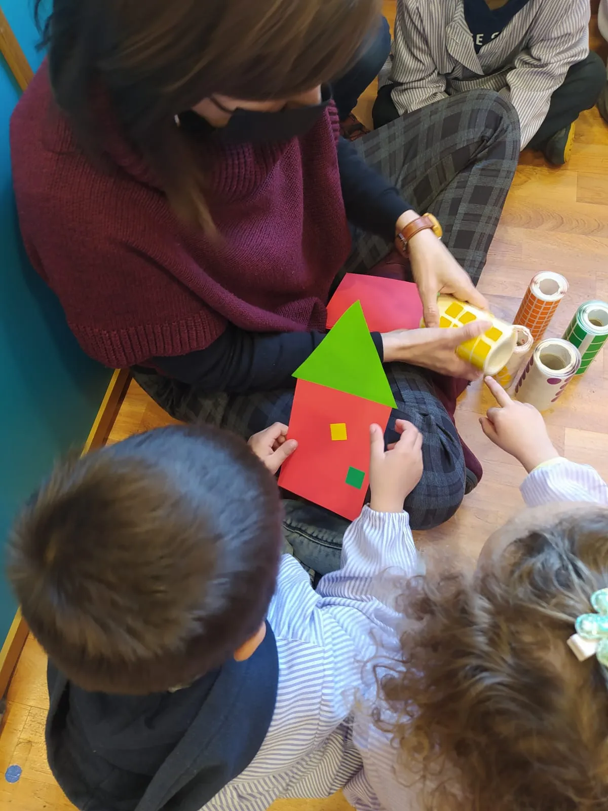 Infants ajupits a terra fent una casa de cartolina amb colors.