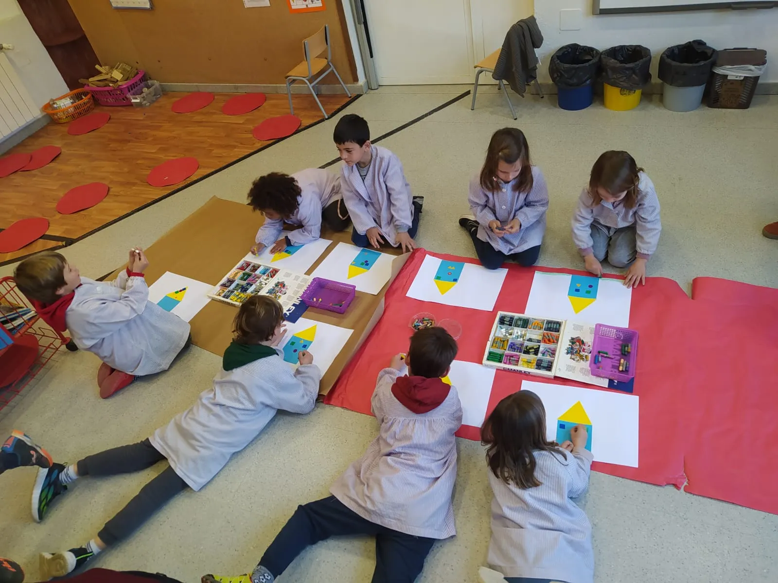 Infants estirats a terra sobre papers de colors construint cases.
