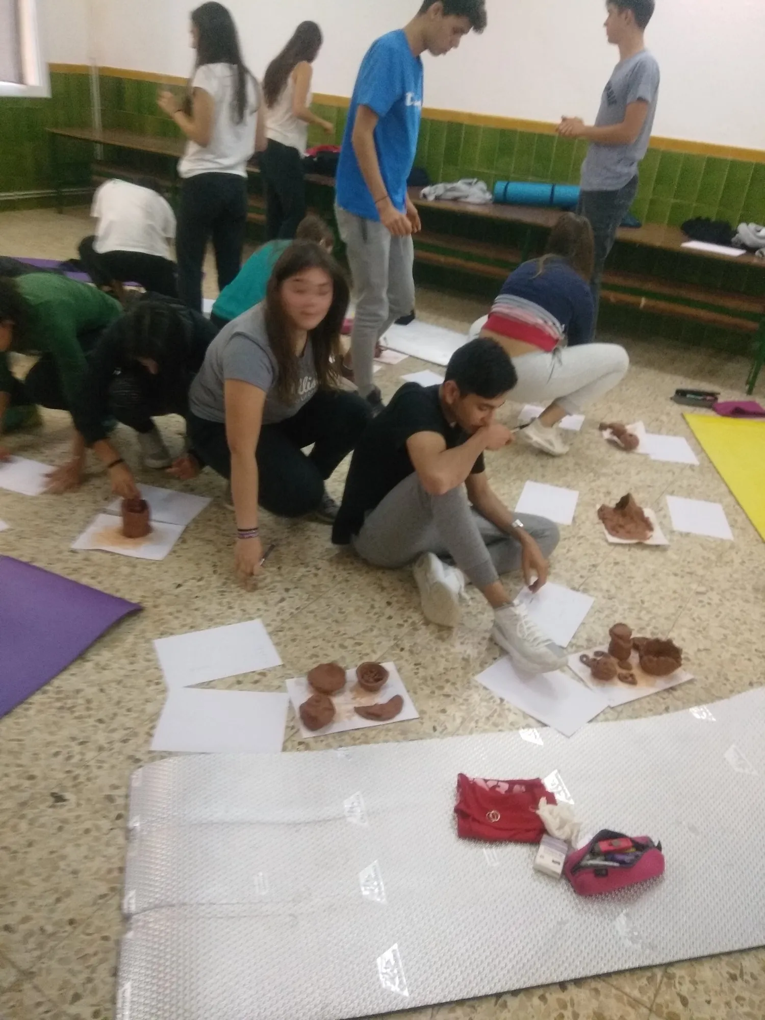 Alumnes treballant amb fang sobre papers estesos a terra.