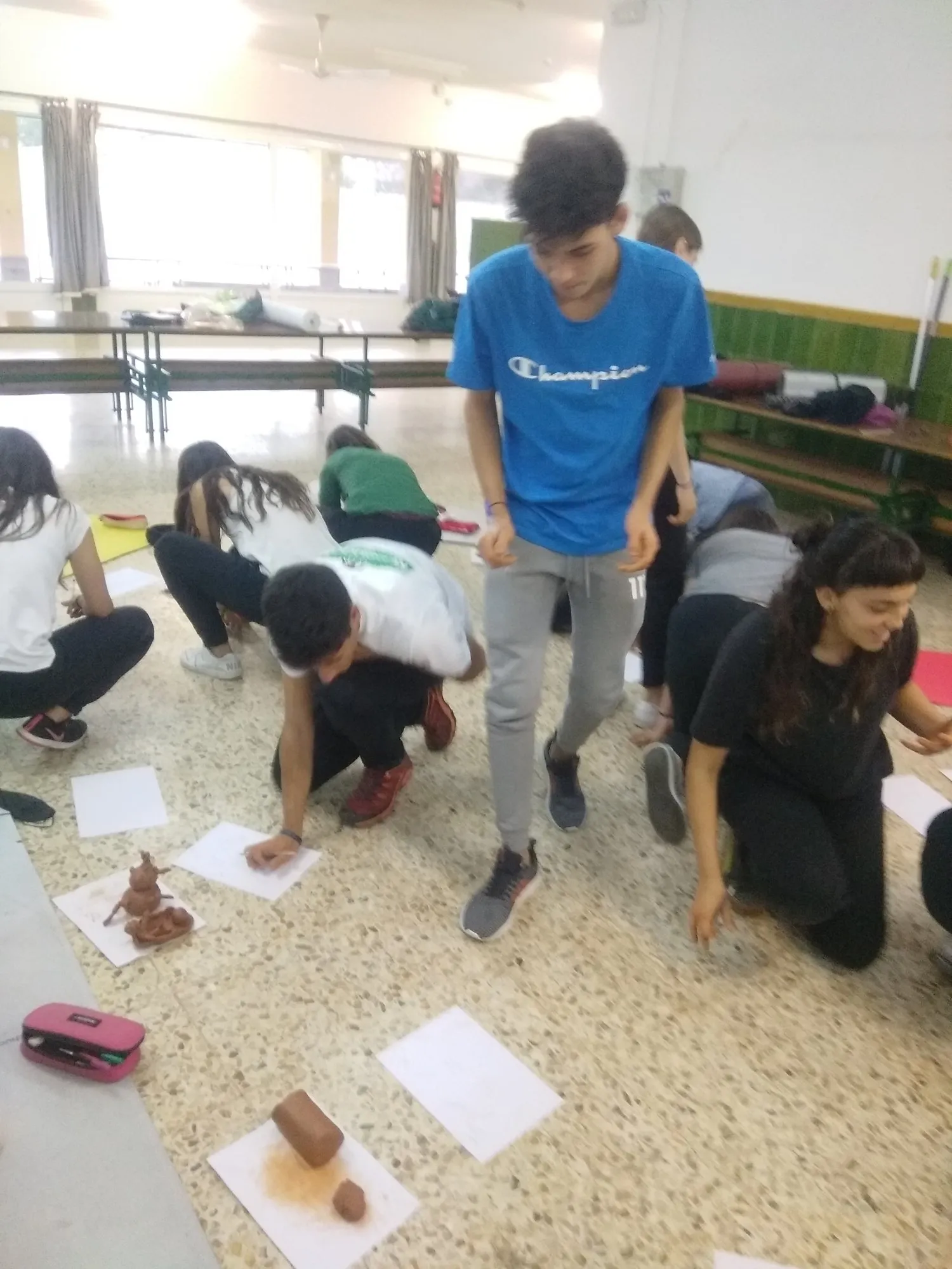 Grup d'alumnes a terra amb les seves figures de fang mentre un noi s'hi apropa.