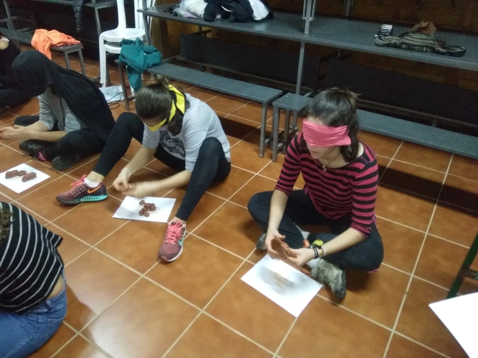 Dues alumnes amb els ulls embenats amb un mocador modelant fang a terra.